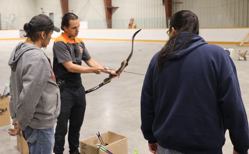 Harold Angeconeb coaching a youth in archery with his great uncle watching