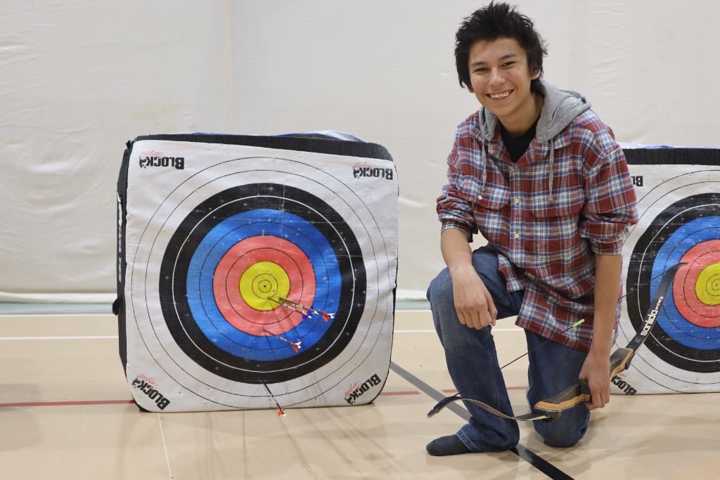 Youth archer beside bullseye target in gym